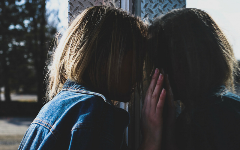 A woman presses her head and hands against a reflective surface.