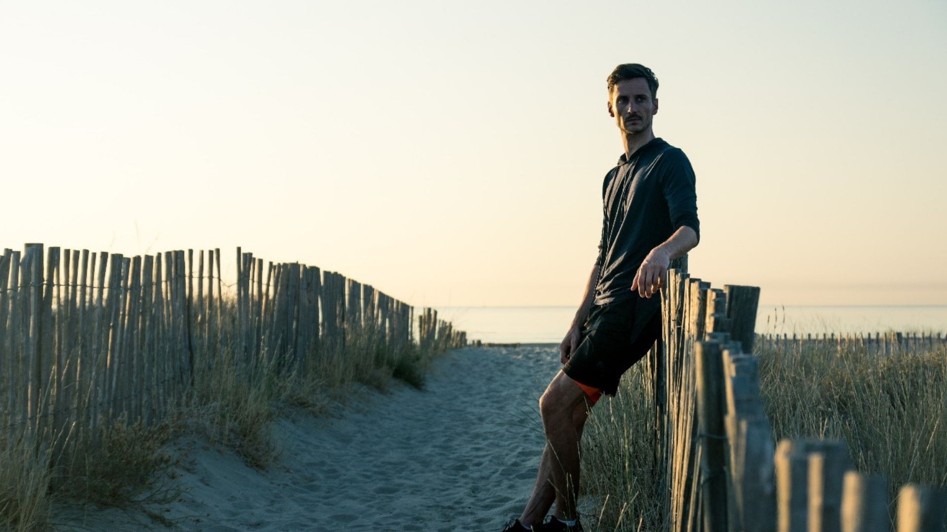 man leaning on beach fence