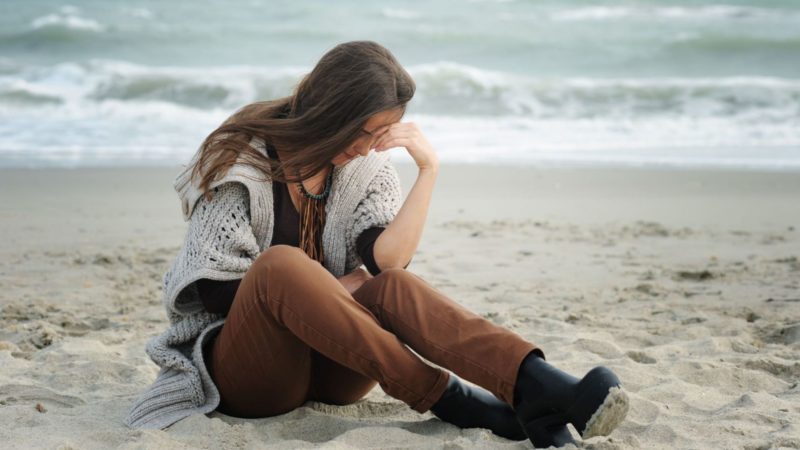 young woman sitting on beach with her head down