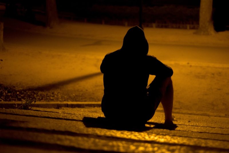 man sitting on a dark sidewalk